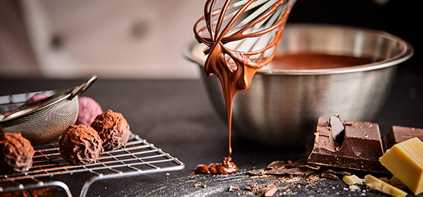 a chocolatier with a wish oozing chocolate onto a counter with confectioneries and chocolate pieces next to it